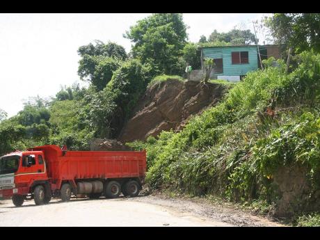 Credit: Photo by Bryan Miller A crew contracted by the National Works Agency clearing a land slippage from the main road in Johnson Town, Hanover, on Wednesday. Residents in precariously perched homes say they have nowhere to go.