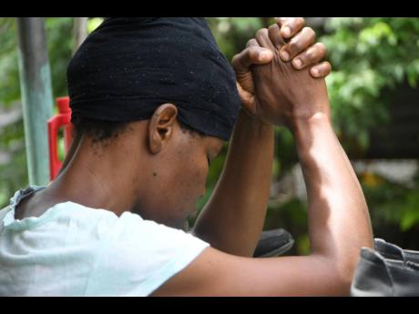 Carolyn Smith in prayerful contemplation on Monday. Her son is on the run in relation to the death of his uncle, Joseph Smith, in Sandy Park, St Andrew. 