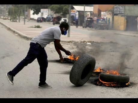 A supporter of former Senator Youri Latortue and Steven Benoit sets fire to tyres outside of Haiti’s courthouse in Port-au-Prince on Monday, July 12, where high-profile politicians were being questioned as part of the investigation into the assassination