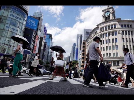In this August 10, 2021, file photo, people wearing face masks to help curb the spread of the coronavirus walk under the scorching sun in the Ginza Shopping district in Tokyo. 
