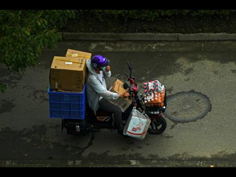 A delivery worker rides on an electric-powered scooter loaded with parcels and beverages on a street in Shanghai, China, on Monday, August 16. 