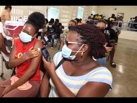 Nicole Samuels takes pictures of her daughter Natasha after she was vaccinated by registered midwife Ann-Marie Amos at St George's College on Saturday.