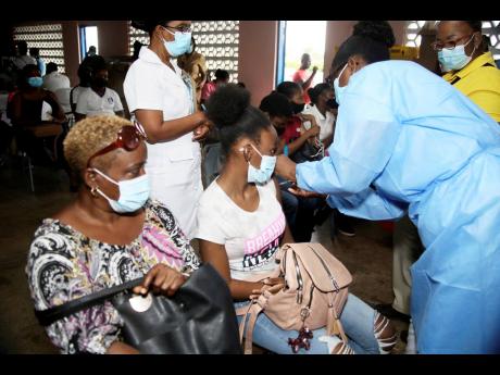 Credit: Nathaniel Stewart/Photographer Nurse Henry of the Clarendon Health Department administers the first dose of the COVID-19 vaccine to Nicola Johnson of May Pen Academy while her mother, Michelle Israel, looks on during the vaccination blitz targeting students at Denbigh Primary School on