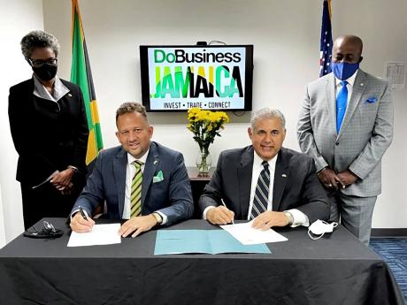 Sharon Burrell (standing at left), deputy consul general at the Consulate  General of Jamaica in Miami, and Vance Carter (standing at right), vice-consul, look on as Oliver Mair (seated, left), consul general in Miami, and Anthony Barbar sign the memorandu