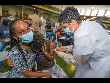 Ann-Margaret Lim (left) holds her daughter Kayla Kerr as she is vaccinated by public health nurse Sashagaye Johnson at the National Arena on Tuesday. 