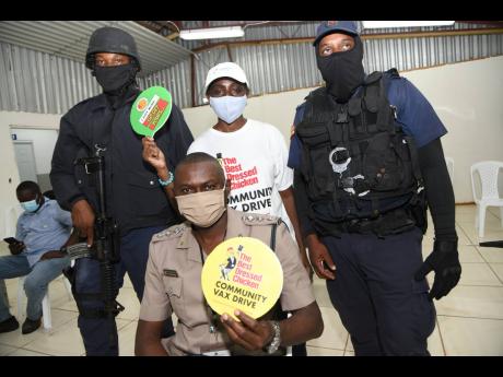 Jennifer Chin (second left standing), an employee of Best Dressed Chicken with (from left) Constable Kemar James, Superintendent Mark Harris and Corporal Layton Hutchinson, after they got their vaccine at the Best Dressed Chicken vaccination drive.