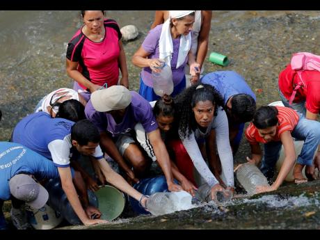 
People collect water falling from a leaking pipeline on the bank of the Guaire River during rolling blackouts, which affects access to running water in Caracas, Venezuela, in this March 2019 photo. The blackout has intensified the toxic political climate,
