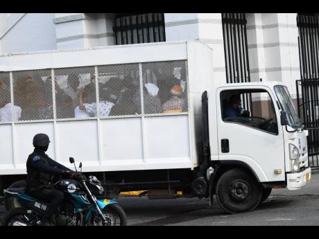 A motorcycle cop keeps a watchful eye on a police truck with some of the alleged members of the One Don faction of the Clansman Gang near the precincts of the Home Circuit Court on Monday.