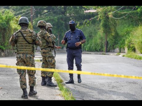 A cop engages in dialogue with soldiers at the scene where reputed gang leader Christopher Linton, more popularly known as 'Dog Paw', was shot and killed in an alleged confrontation with the police in Elletson Flats, eastern St Andrew, on Monday. 