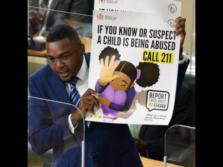 Robert Nesta Morgan, state minister in the Ministry of Education, shows a child-abuse poster in Parliament on Tuesday. The Clarendon North Central MP was making his debut contribution to the State of the Constituency Debate.