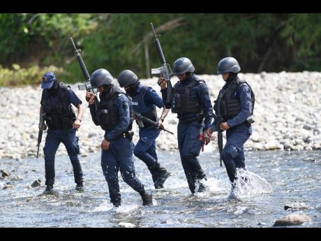 Policemen on the hunt for Davian Bryan and the missing Winshae Barrett crossing the Plantain Garden River in St Thomas on Sunday.