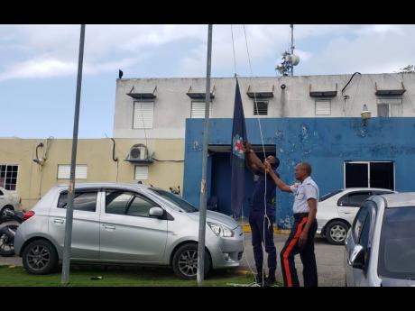 Policemen raise the Jamaica Constabulary Force flag at half staff in honour of the late Constable Orlando Irons at the Freeport Police Station in Montego Bay on Monday. Irons and disgraced pastor Kevin O. Smith succumbed to crash-related injuries. 