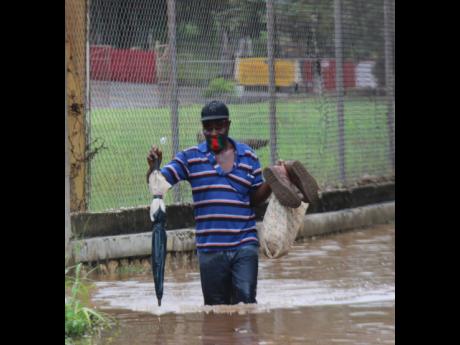 Credit: Ashley Anguin/Photographer A man walks across a flooded Orange Street in Montego Bay on Monday. Several roadways were flooded and damaged in the city.