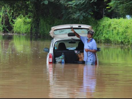 Credit: Ashley Anguin/Photographer Peter Dawson, a taxi operator, is trapped in floodwaters on Orange Street in Montego Bay after heavy rainfall on Monday. Firefighters subsequently assisted him in removing his vehicle.