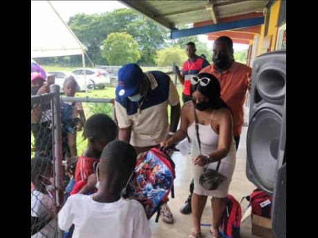 Dave Johnson (in blue cap) assists in handing out school bags to students at the Fullerswood Primary and Infant School in St Elizabeth recently.   
