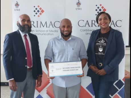 Credit: Contributed Outstanding CARIMAC master’s graduate Kaneal Gayle with a symbolic cheque he received from Shanoy Coombs, CEO of Infinity IMC ( right), as CARIMAC director Livingston White looks on.