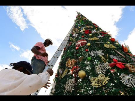 Mervin Murray (left) hands Daniel Simmonds Christmas lights as the two labour on decorating the Gregory Park Christmas tree sited along the community's main road in St Catherine on Sunday. The decorators sought to bring holiday cheer to the Portmore commun