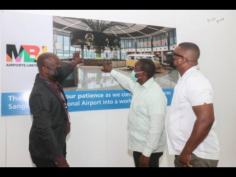 Shane Munroe (left), CEO of MBJ Airports, shows Transport Minister Robert Montague (second right) and Central St James Member of Parliament Heroy Clarke a photograph of the new departures retail shopping area during a tour of the Sangster International Air