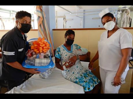 Cleon Insang, representative of Kirk Distributors, in keeping with the company’s tradition of gift-giving to the firstborn on New Year’s Day, presents Sharona Nelson with a gift package, as Annastacia Rose, ward manager and acting deputy director of nu