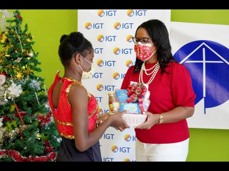 After performing an electrifying dance with her peers, this young lady from the Mustard Seed Communities – Jerusalem! children’s home in St Catherine, collects a gift basket from General Manager of IGT  Debbie Green at the My Jamaican Christmas event h