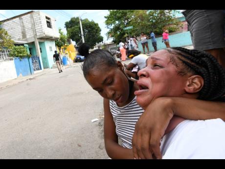 An unidentified woman comforts Danielle Robinson after her cousin, Quacie Harriott, was allegedly shot dead by the police at his Zacky Avenue home in Tivoli Gardens, western Kingston, on Monday. The police claimed to have taken a loaded weapon from his bod