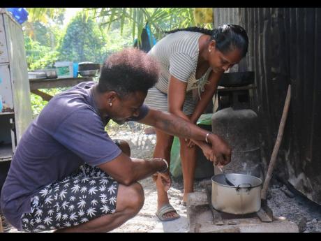 Credit: Ashley Anguin Jeffery and Rozanna Barron prepare a meal on a makeshift stove at their father’s temporary home in Dumfries, Trelawny.