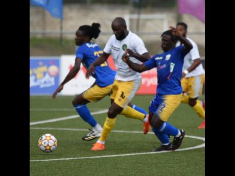 Vere United's Francois Swaby (centre) fights off the attention of Molynes United's Jevaughn Brown (right) during their Jamaica Premier League game at the UWI-JFF Captain Horace Burrell Centre of Excellence this evening. Vere won the game 1-0.  