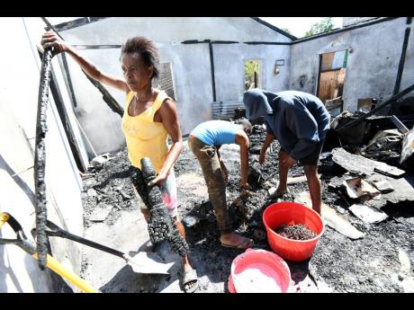 Fire victims cleaning up after a house burned down on White Lane in Naggo Head, Portmore, on Wednesday. Fifteen persons were displaced by the blaze. 