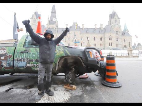 A man who removed the tires from his pickup truck stands in front of West Block on Parliament Hill as a rally against COVID-19 restrictions. The truckers’ demonstration, which began as a cross-country convoy protesting a federal vaccine mandate for truck