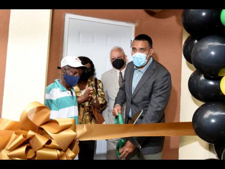 Prime Minister Andrew Holness cuts the ribbon to a new house on Grands Pen Avenue in St Andrew on Wednesday, that was handed over to Lloyd Edwards (left). The Prime Minister was accompanied by Member of Parliament for St Andrew North Easter Delroy Chuck (s