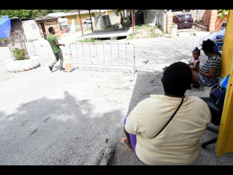 Credit: Rudolph Brown/Photographer Residents sit near a security checkpoint in Goldsmith Villa yesterday. The build phase of the zone of special operations has formally began in parts of August Town such as Goldsmith Villa and African Gardens.
