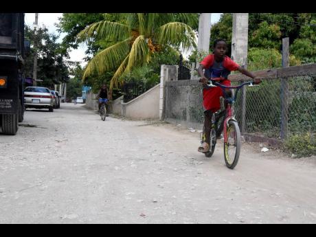 Two boys from Dunbeholden in St Catherine ride their bicycle along the unpaved Gilbert Avenue. The majority of the roads in the community are unpaved which has caused a constant dust nuisance.
