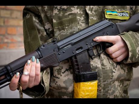 An armed civil defence woman holds a Kalashnikov assault rifle while patrolling an empty street due to a curfew in Kyiv, Ukraine. A Ukrainian official says street fighting has broken out in Ukraine’s second-largest city of Kharkiv. Russian troops also pu
