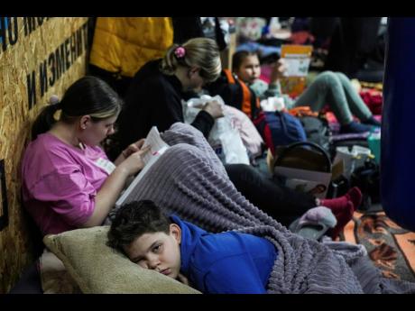 People lie on the floor in the improvised bomb shelter in a sports centre, which can accommodate up to 2000 people, in Mariupol, Ukraine, on Sunday. Below: A woman and her children in the bomb shelter.