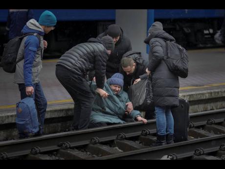 
A woman gets help after falling on the tracks trying to reach a Lviv bound train, in Kyiv, Ukraine.