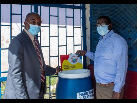 Everton Anderson (right), chief executive officer, National Health Fund (NHF), stands with Donovan Hunter, principal of the Denham Town High School, at the foot-pedal handwash station donated to the school in assisting with reopening efforts. The station w