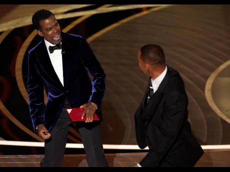Credit: AP Presenter Chris Rock (left), reacts after being hit on stage by Will Smith while presenting the award for Best Documentary Feature at the Oscars on Sunday. Smith resigned Friday from the motion picture academy and said he would accept any further punishmen