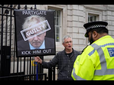 A police officer talks to a protester holding up a sign showing British Prime Minister Boris Johnson, in front of the entrance to Downing Street in London, yesterday. 