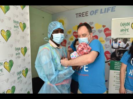 Tajay Mason (left) hands his seven-month-old daughter Kaile to consultant paediatric cardiologist Dr John Thomson yesterday at the Bustamante Hospital for Children in Kingston. Kalie is recovering from her third heart procedure, the latest of which was don