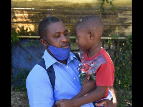 Credit: Ashley Anguin/Photographer Jason Bryan Sr holds five-year-old son, Jeremiah, in Gutters, St James, on Tuesday. Eleven-year-old Jason Bryan Jr, the elder brother, was mowed down by a car on Mother’s Day in the community. He succumbed to his injuries at hospital on Monday.