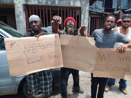 Credit: Photo by Hopeton Bucknor Placard-bearing residents protest deplorable road conditions in the Westmoreland Central and Eastern constituencies on Monday.