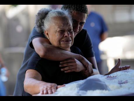 Divone Ferreira da Cunha, 74, and her grandson mourn next to the body of her daughter Gabrielle Ferreira da Cunha, 41, who was killed during a police raid in the Vila Cruzeiro favela, during her funeral in Rio de Janeiro, Brazil yesterday. Police raided th