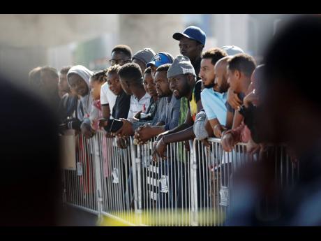 In this 2019 photo, people wait to apply for asylum in the United States along the border in Tijuana, Mexico. Because America promises opportunities, some frustrated Jamaicans will leave good, middle-class jobs here and clean toilets and tend to sick peopl