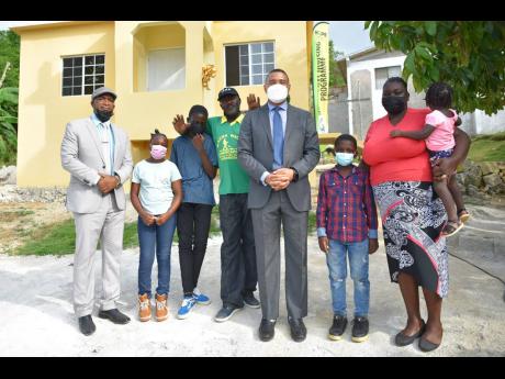 Prime Minister Andrew Holness (fourth right), and Member of Parliament for St Elizabeth North Eastern, Delroy Slowley (left), share a moment with Courtney (fourth left), Topal Williams (second right) and their children at the handover of a new three-bedroo