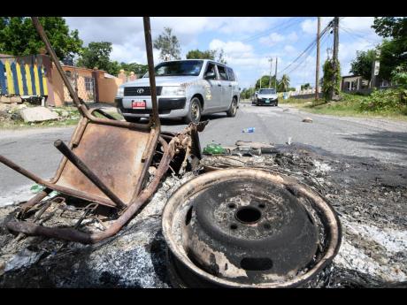 Credit: Rudolph Brown
Motorists drive around roadblocks in Spanish Town last Wednesday. Residents mounted barricades to limit the threat of drive-by gun attacks.