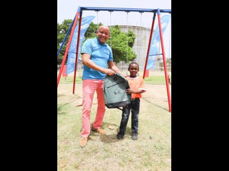 Mark Chisholm, executive vice-president, sales - Individual Life Division, Sagicor Life, presents a backpack to a student of the Iris Gelly Primary School in Arnett Gardens, Kingston, following the Sagicor 
Foundation’s handover of playground equipment t
