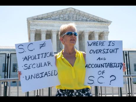 Lynne Damon of Middle River, Maryland, who says she is an independent voter, holds signs questioning the current state of the Supreme Court as she protests outside of the Supreme Court on Wednesday, June 29, in Washington. 
