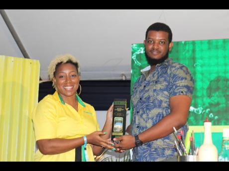 Credit: Stephanie Lyew J. Wray & Nephew White Overproof Brand Manager Sasha Warner hands over a limited-edition Jamaica 60 bottle to Sean Mark Campbell after he answered a trivia question on the brand.