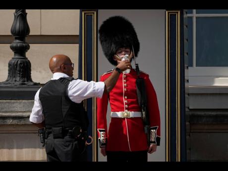 A police officer gives water to a British soldier wearing a traditional bearskin hat, on guard duty outside Buckingham Palace, during hot weather in London on Monday.