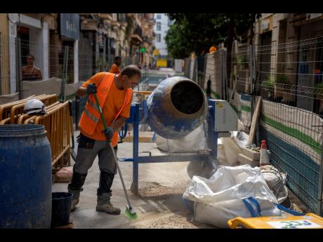 A construction worker cleans the pavement while rehabilitating a street in Barcelona, Spain. The death of a street cleaner during a heatwave in Madrid is driving a debate in Spain about the need to adapt labour rules to the realities of climate change. Mos